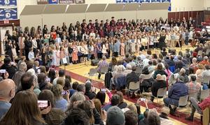 A large choir performance with children and adults on stage in a gymnasium.