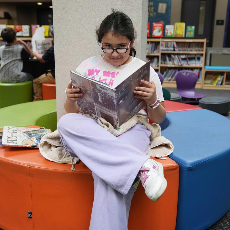 Student sitting on colorful bench reading a book