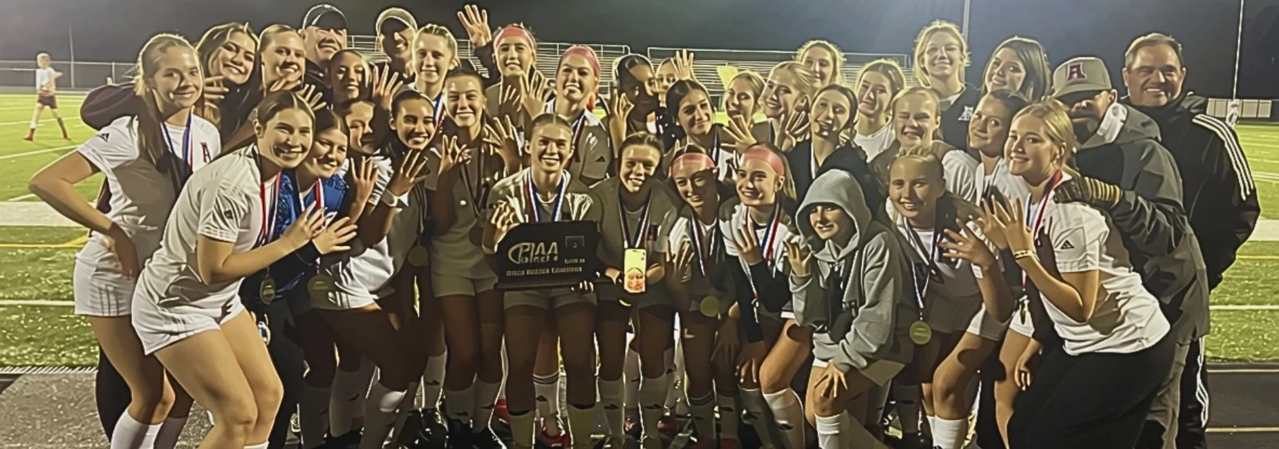 Girls soccer team celebrating a championship win with medals and a trophy.