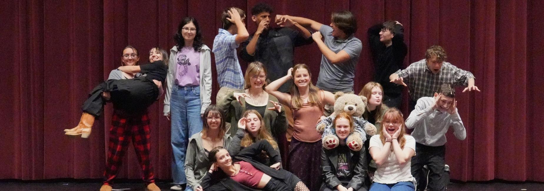 A group of students posing playfully on stage, some holding props.