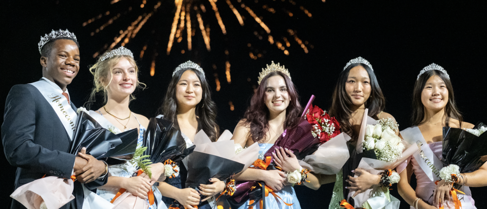 Students who made the homecoming court posing on the football field with fireworks