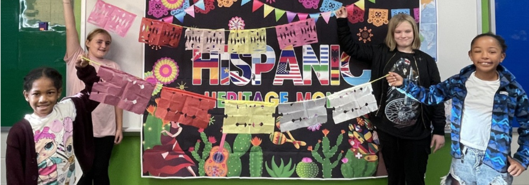 Children holding colorful banners in front of a festive Hispanic Heritage Month backdrop.