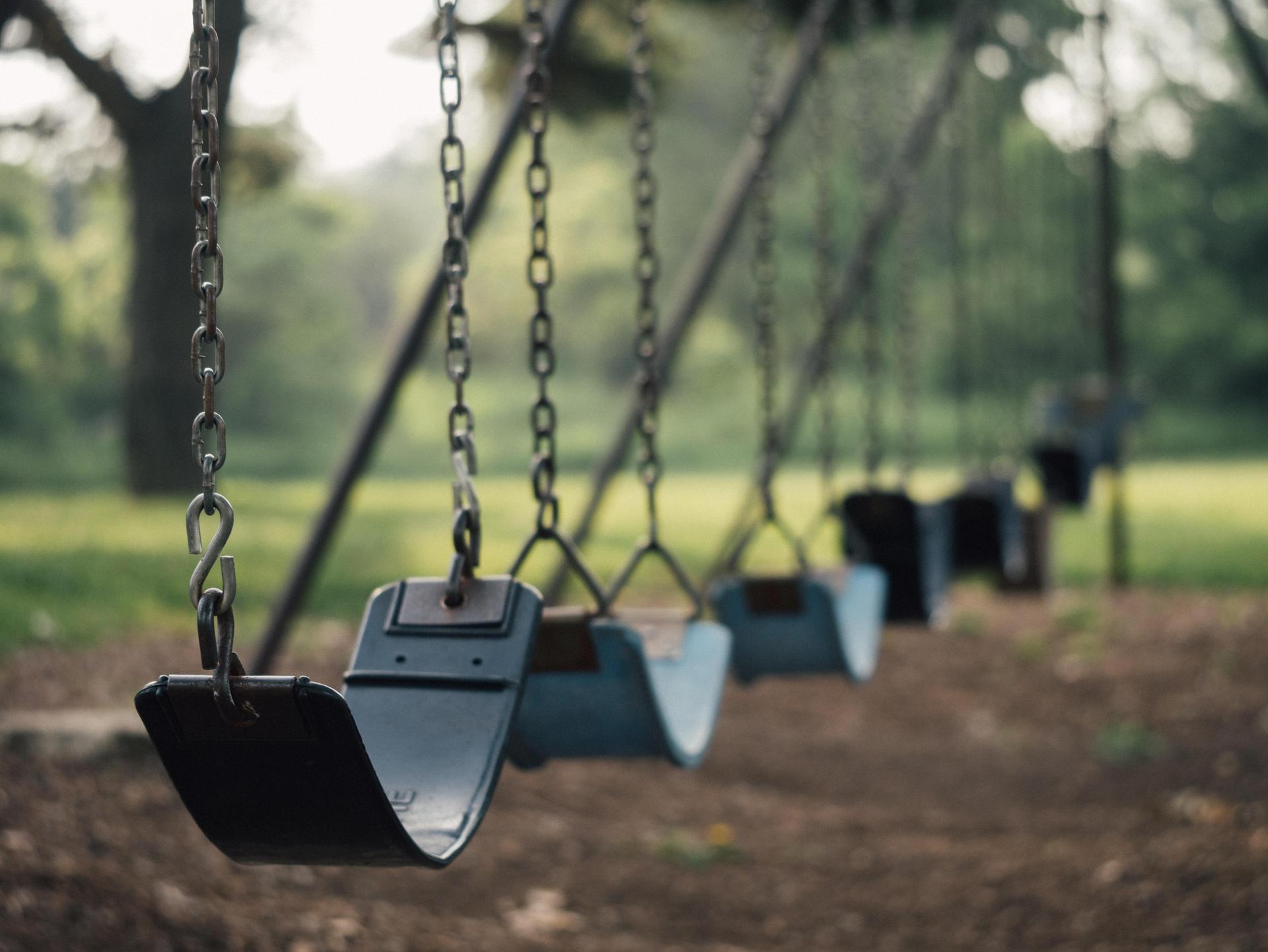 Empty swings in a park with a blurred background of trees and grass.
