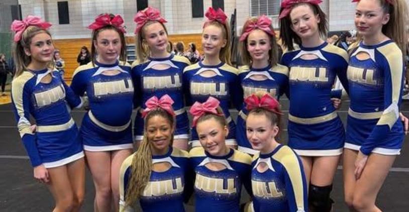 Cheerleading team posing together in blue uniforms with pink bows in their hair.