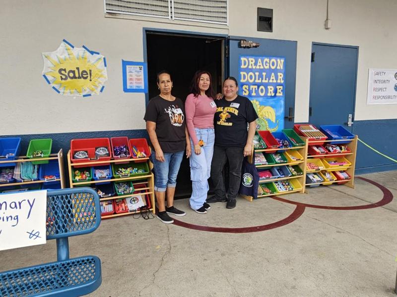 Three women standing outside a school store with shelves of colorful items.