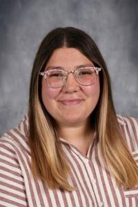 Female teacher with long hair and glasses. Teacher wearing a white and brown stripe shirt