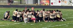 A group of football players kneeling together in a huddle on a grassy field.
