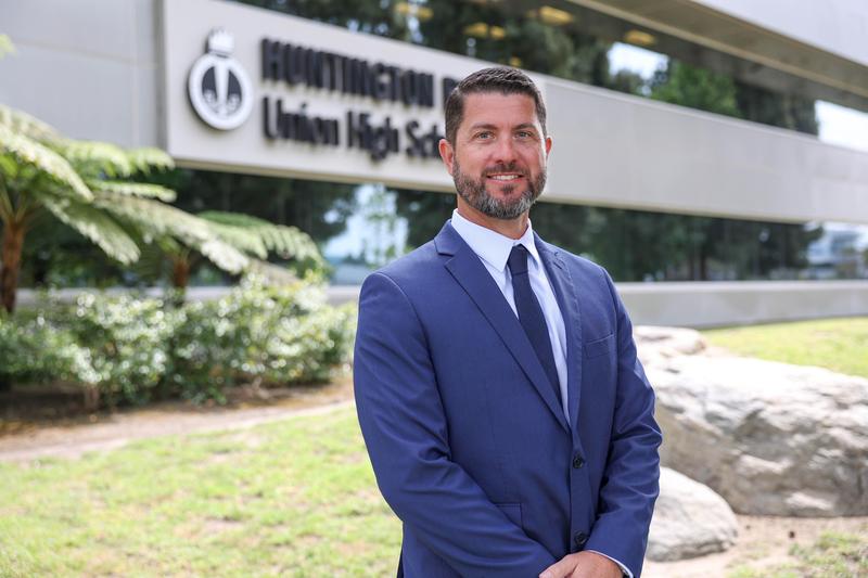 Dr. Smith in a blue suit and tie standing confidently outside Huntington Union High School District on a sunny day.