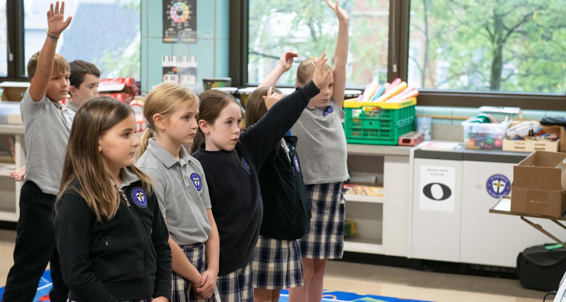 Students in a classroom raising hands, some looking attentive.