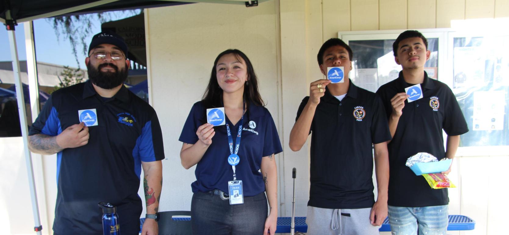 Four people at a table holding stickers and snacks, smiling at the camera.