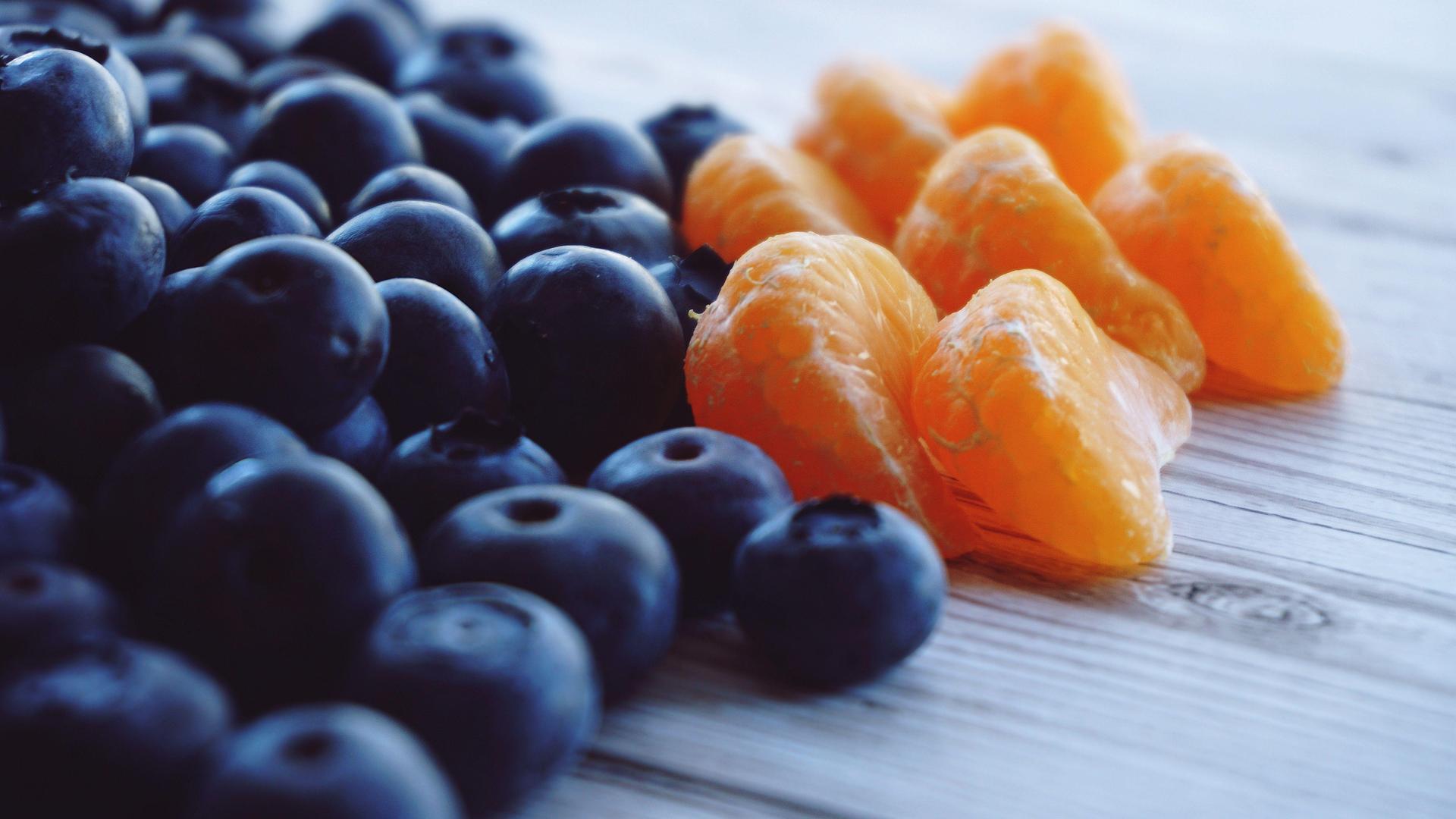 A close-up of blueberries and orange segments on a wooden surface.