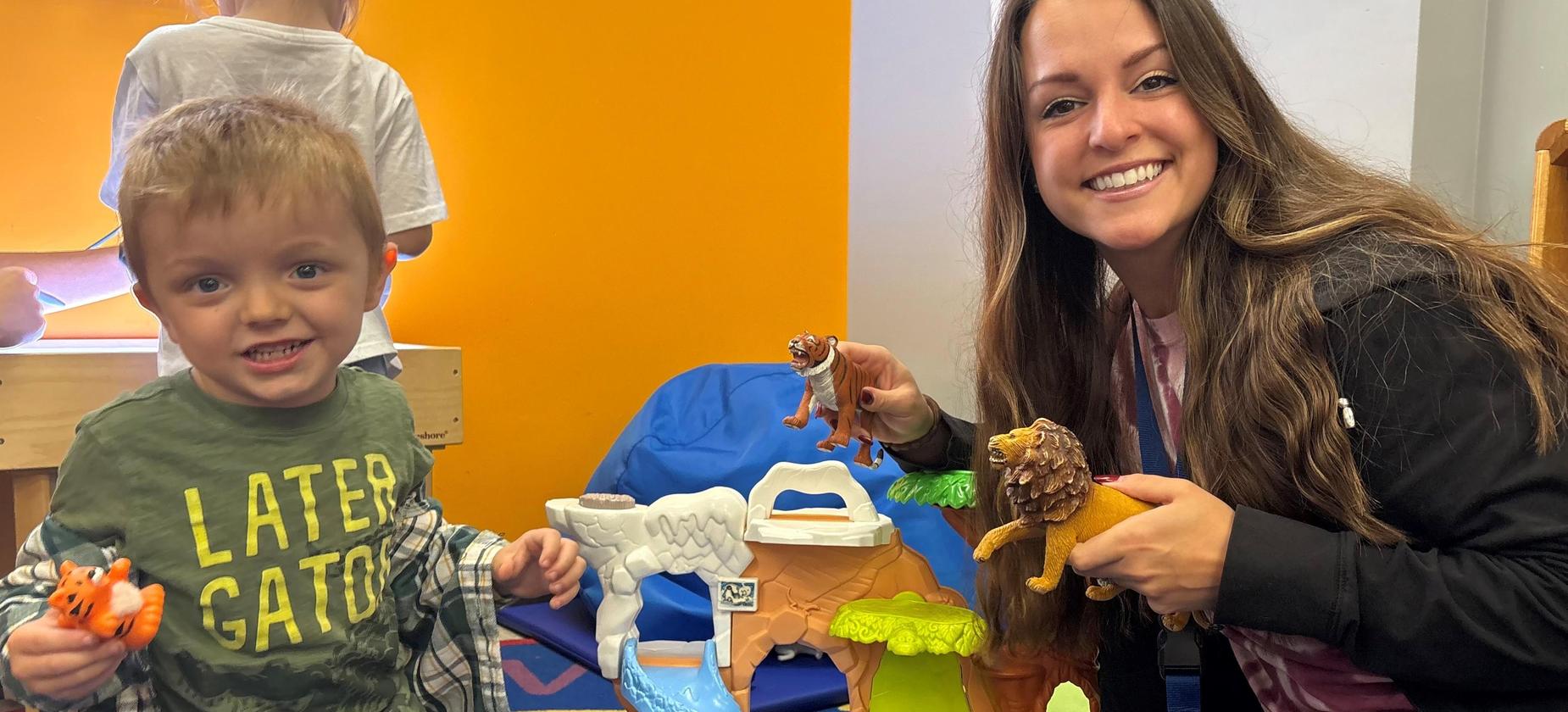Smiling woman and child play with animal toys in a colorful playroom.