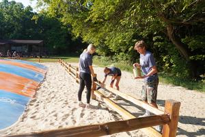 Three students work on staining a split rail fence.