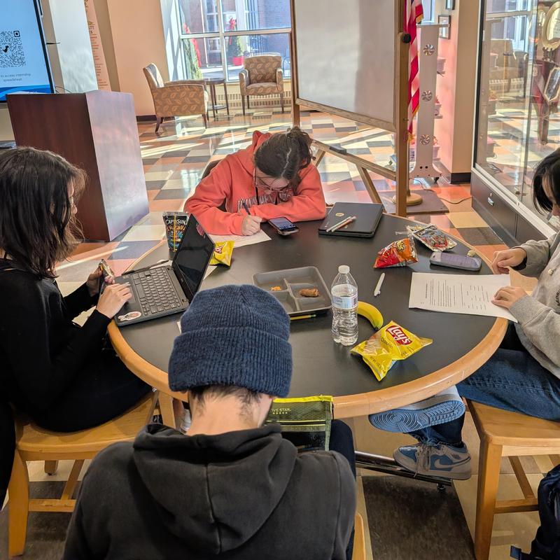 Students studying and snacking around a round table in a library setting.