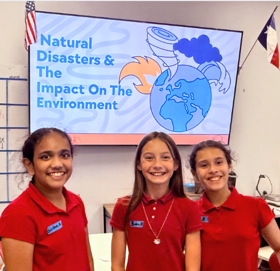 Three students smile in polo uniforms in front of a screen reading, Natural Disasters and the impact on the environment