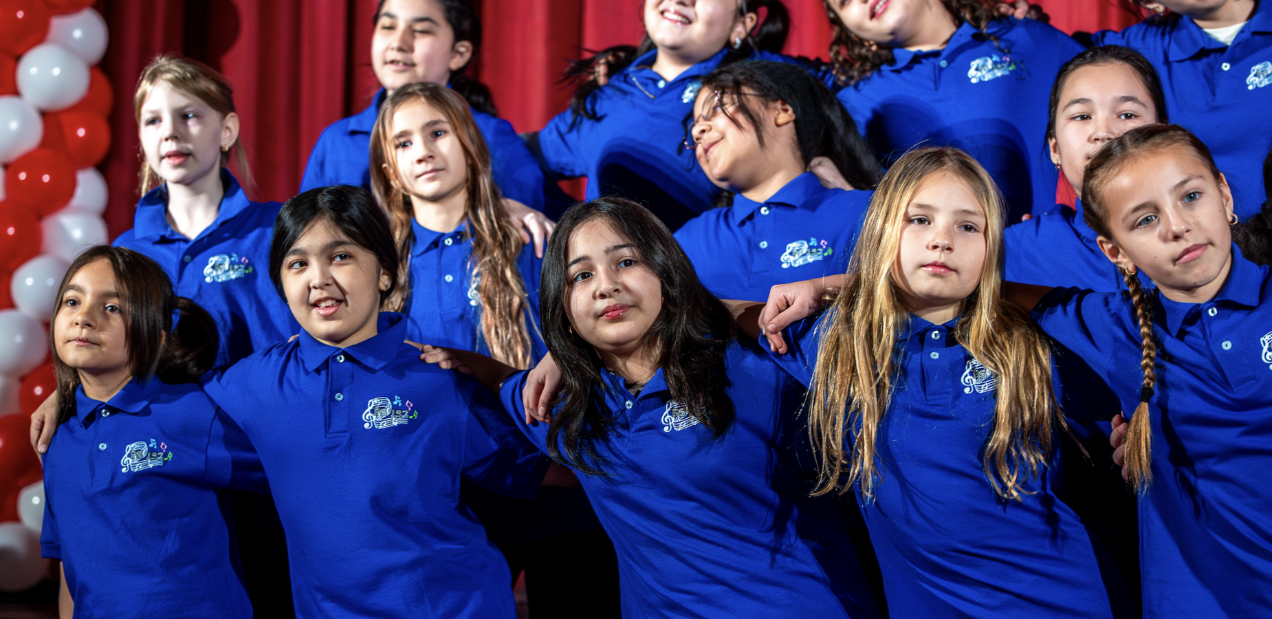 A group of children in blue shirts posing together on stage.