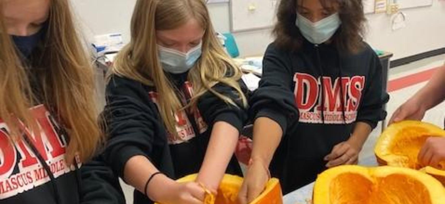 Students clean out a pumpkin in a classroom.