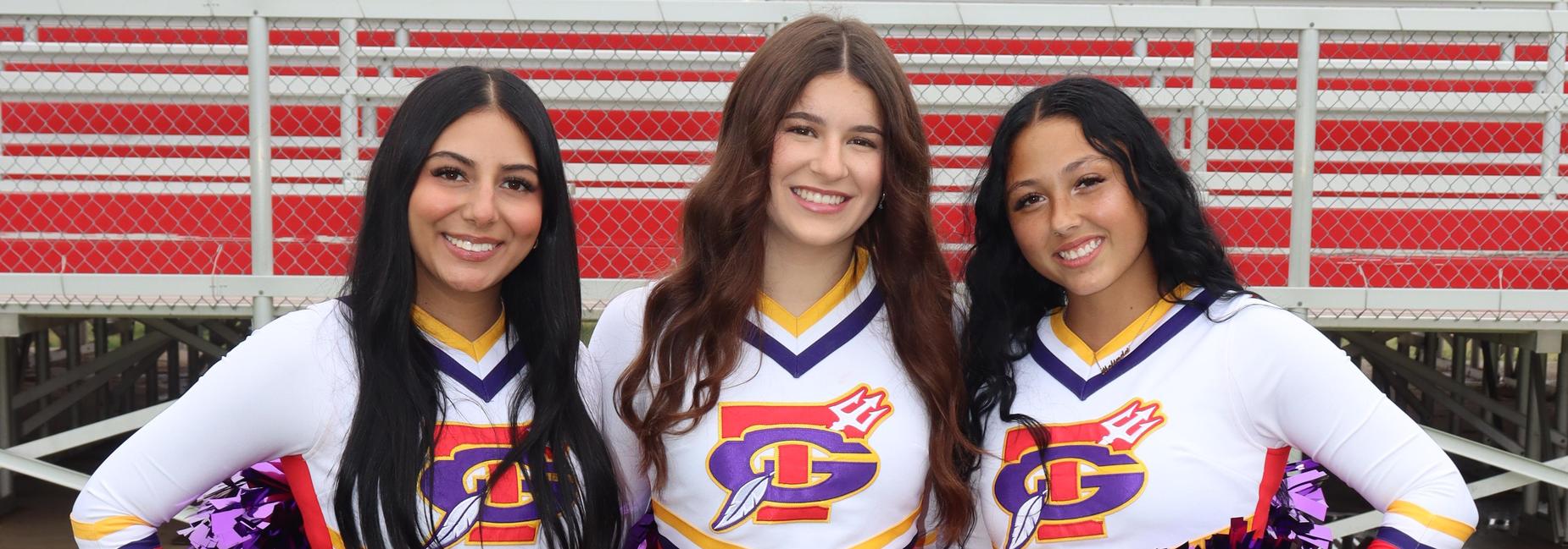 Three cheerleaders in red and yellow outfits with purple pom-poms, standing together.