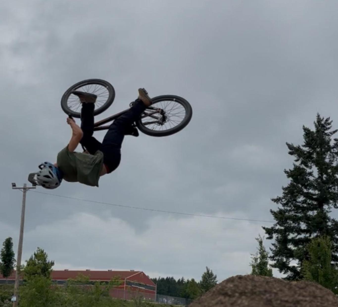 A person performs a bicycle stunt in mid-air over a dirt mound.