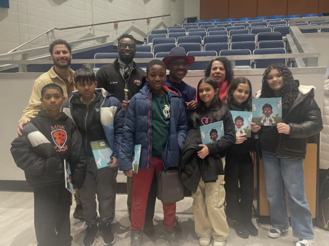 Group of children and adults smiling together, holding booklets at an event.