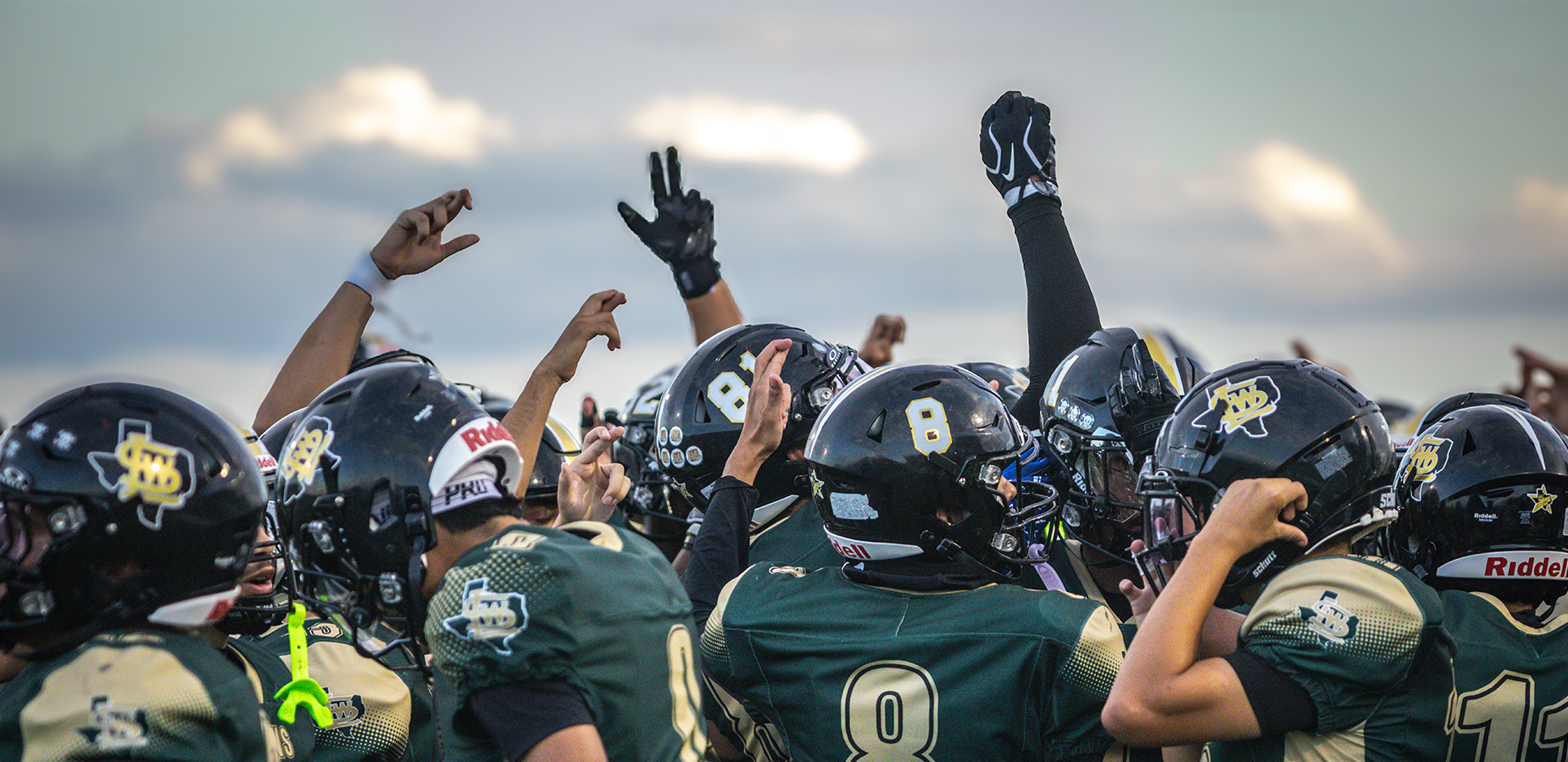 A football team celebrates, raising their arms and helmets in the air.