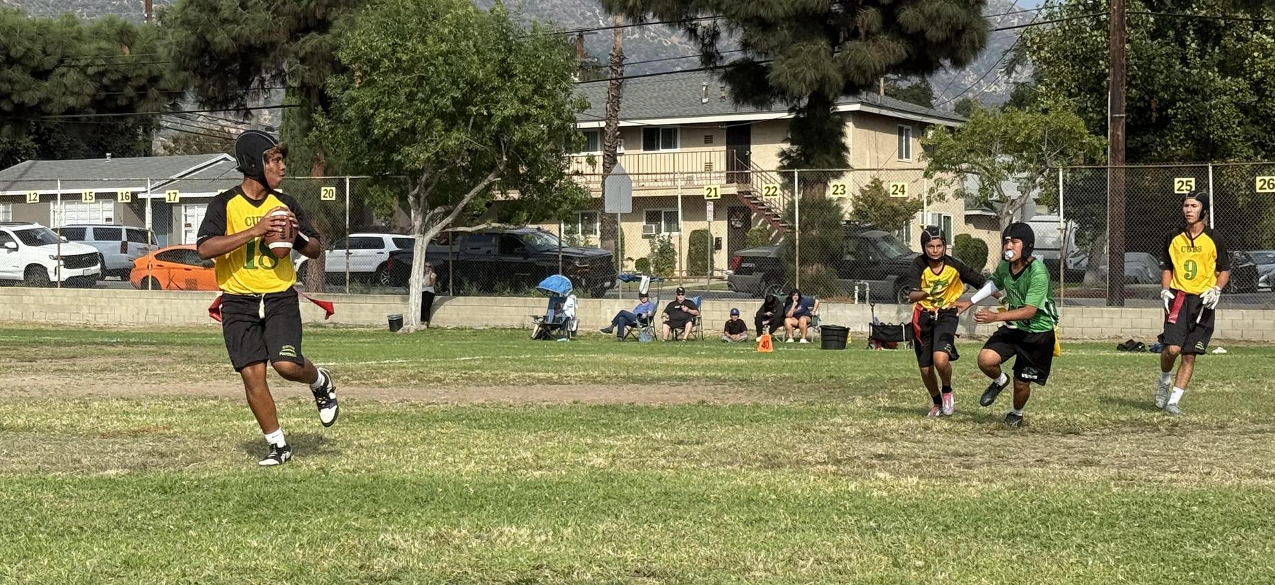 A football player in a yellow jersey prepares to throw while being chased by a defender.