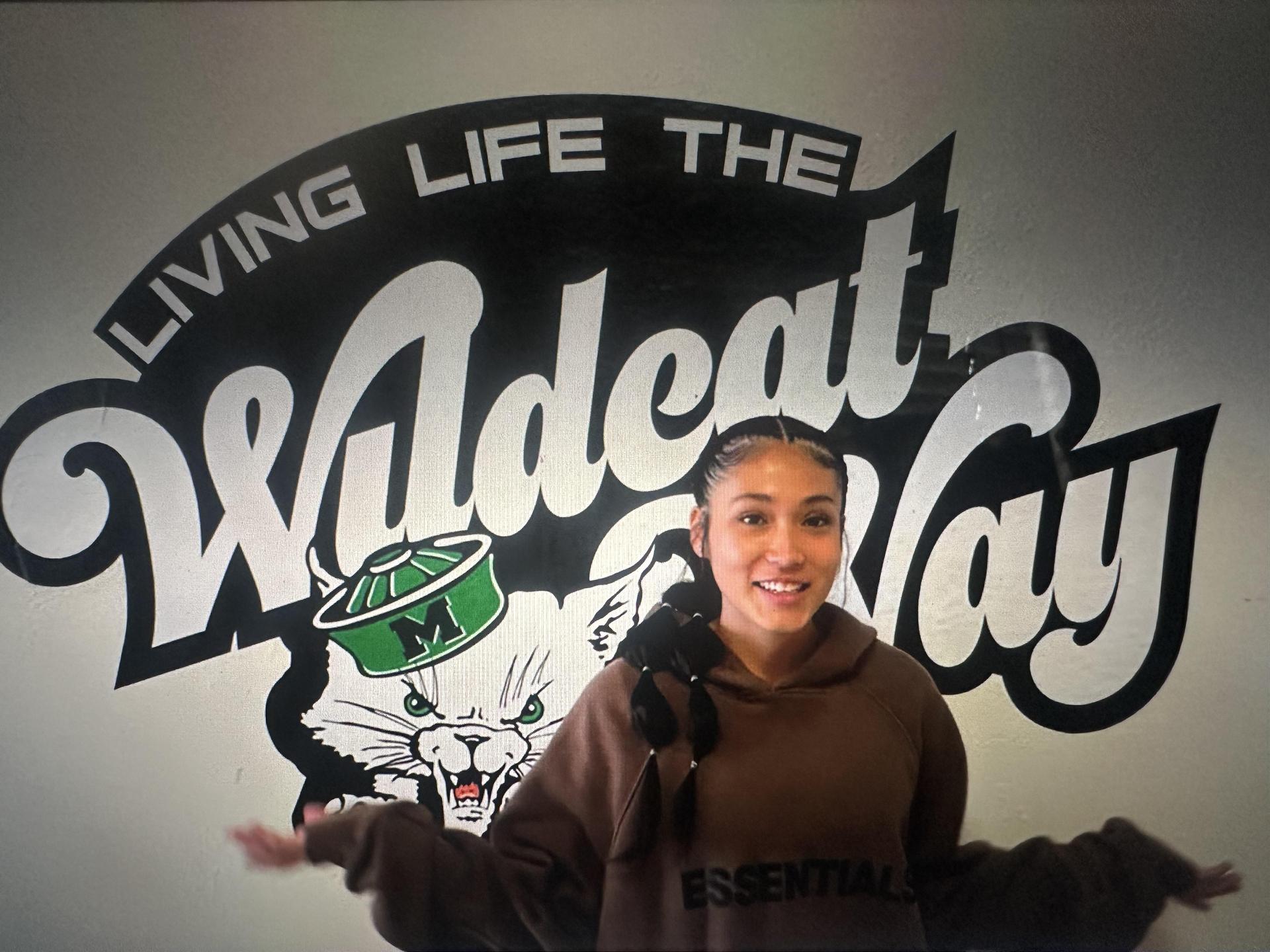 Person smiling with her arms out in front of a high school wildcat logo