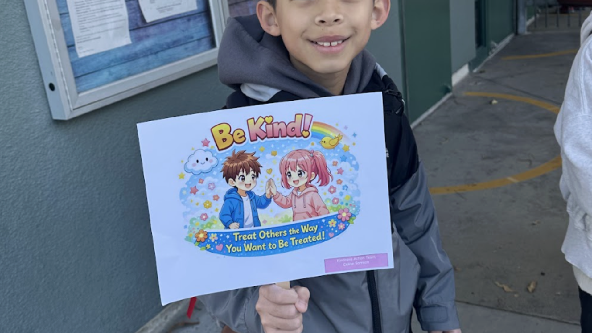 Child holding a sign that reads 'Be Kind!' with colorful cartoon characters.