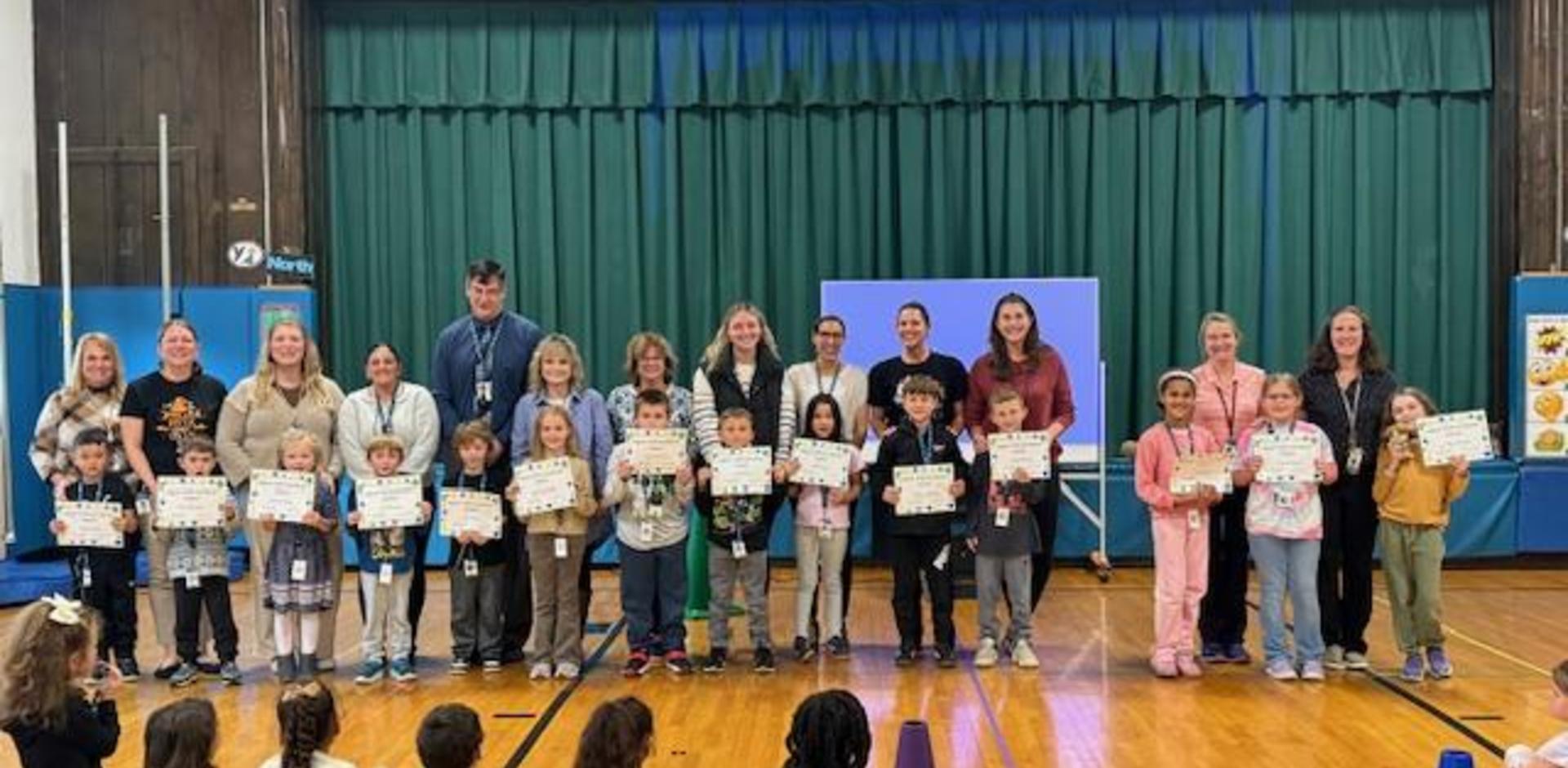 A group of students and adults holding certificates in a school gymnasium.