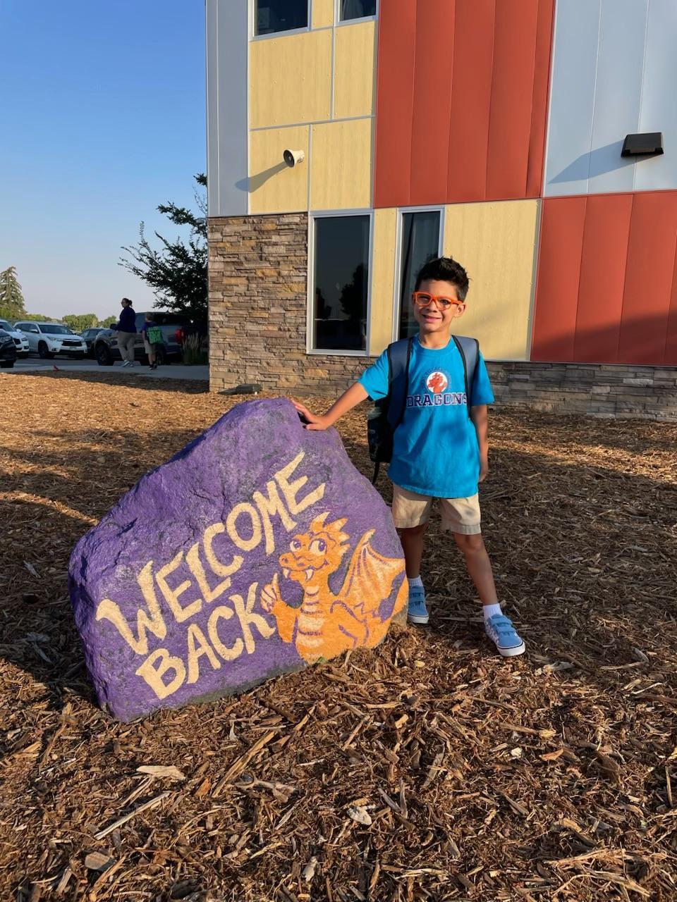 boy with gva shirt standing next to rock that says Welcome Back