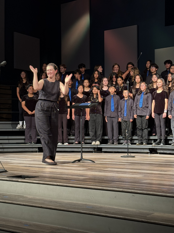 A conductor leads a choir of students on stage during a performance.