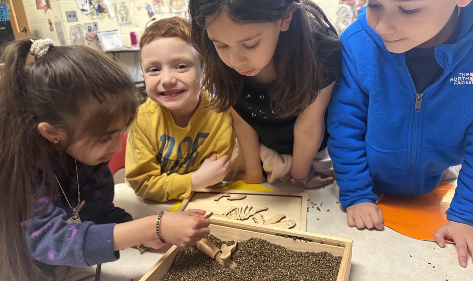 Four children engaging in an activity with a tray of sand and wooden tools.