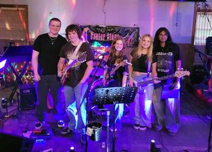 A young band stands together in a colorful stage setting with instruments.