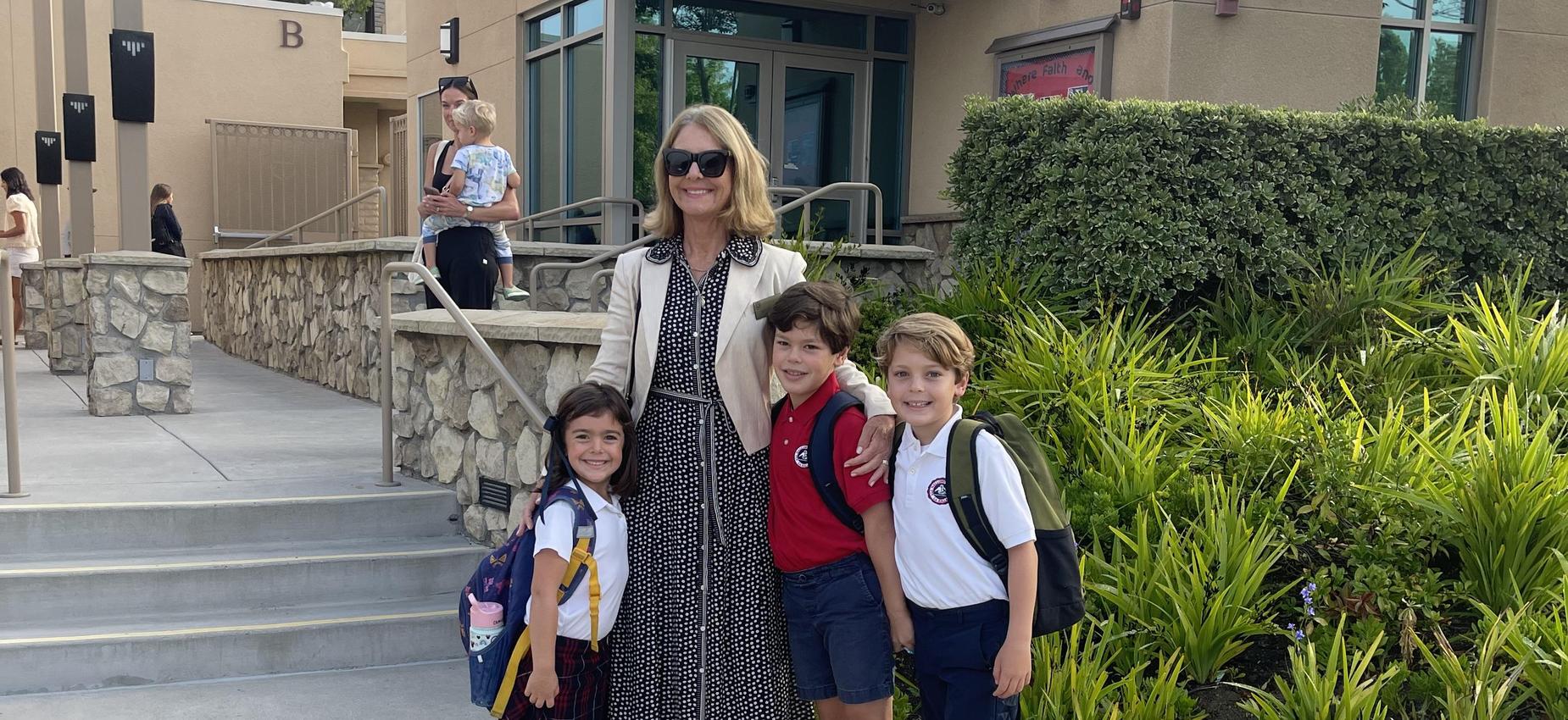 3 students posing in front of school with principal on first day of school