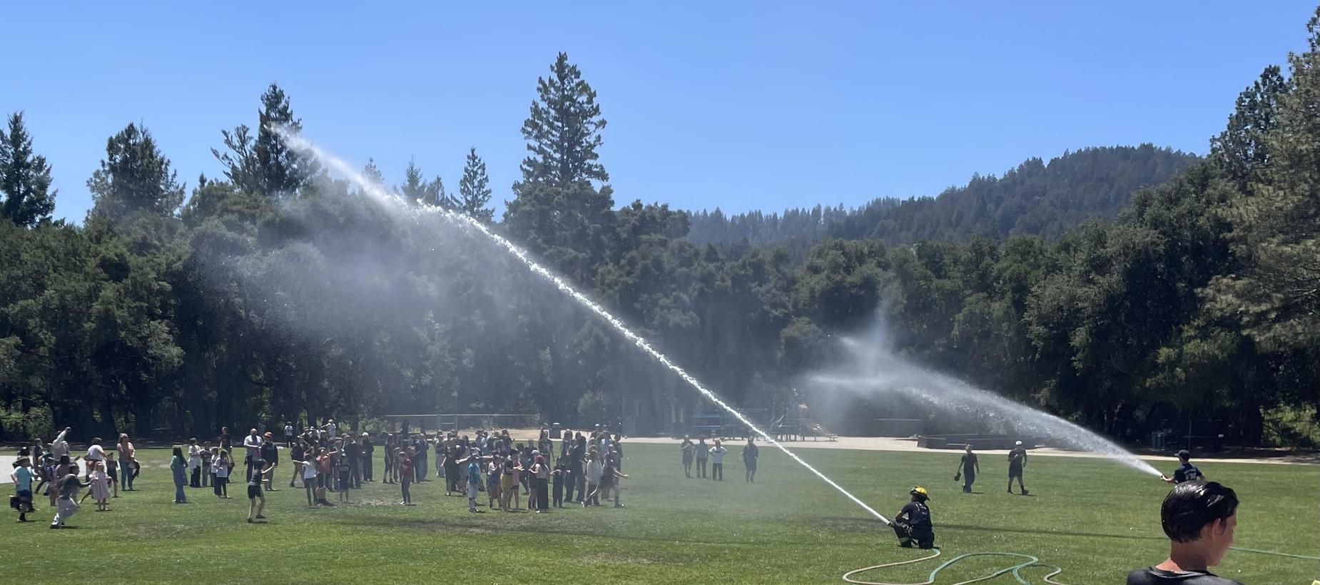 Group of students on Quail Hallow field being sprayed with water by the Ben Lomond Fire Department.