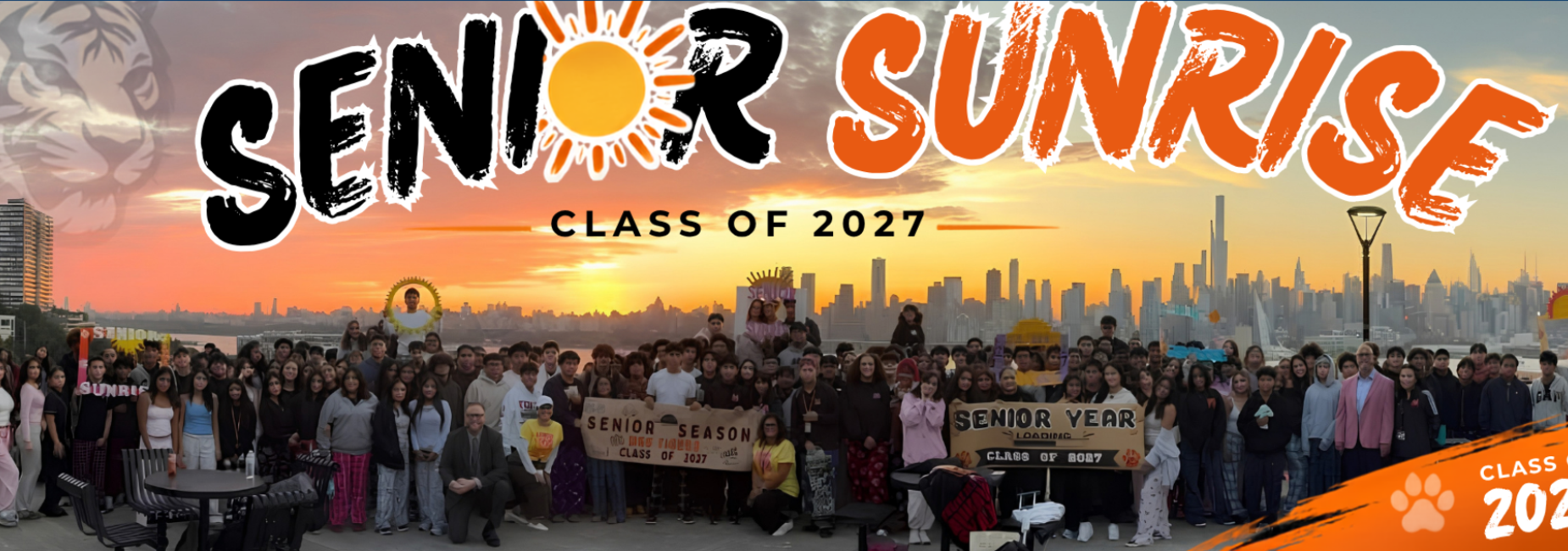 Group of students celebrating Senior Sunrise with banners and city skyline at sunrise.
