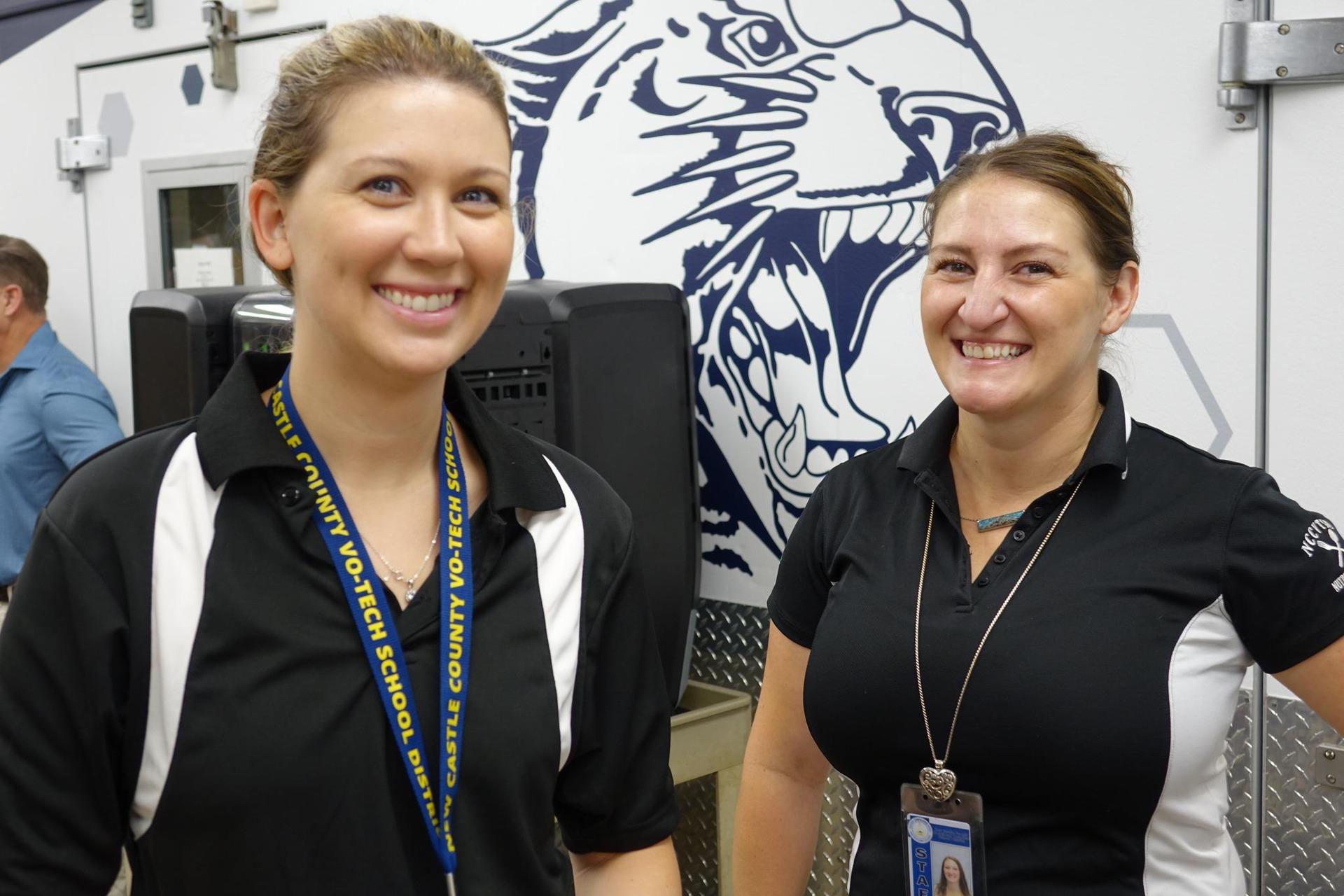 Two women in polo shirts smiling near school-themed decor.