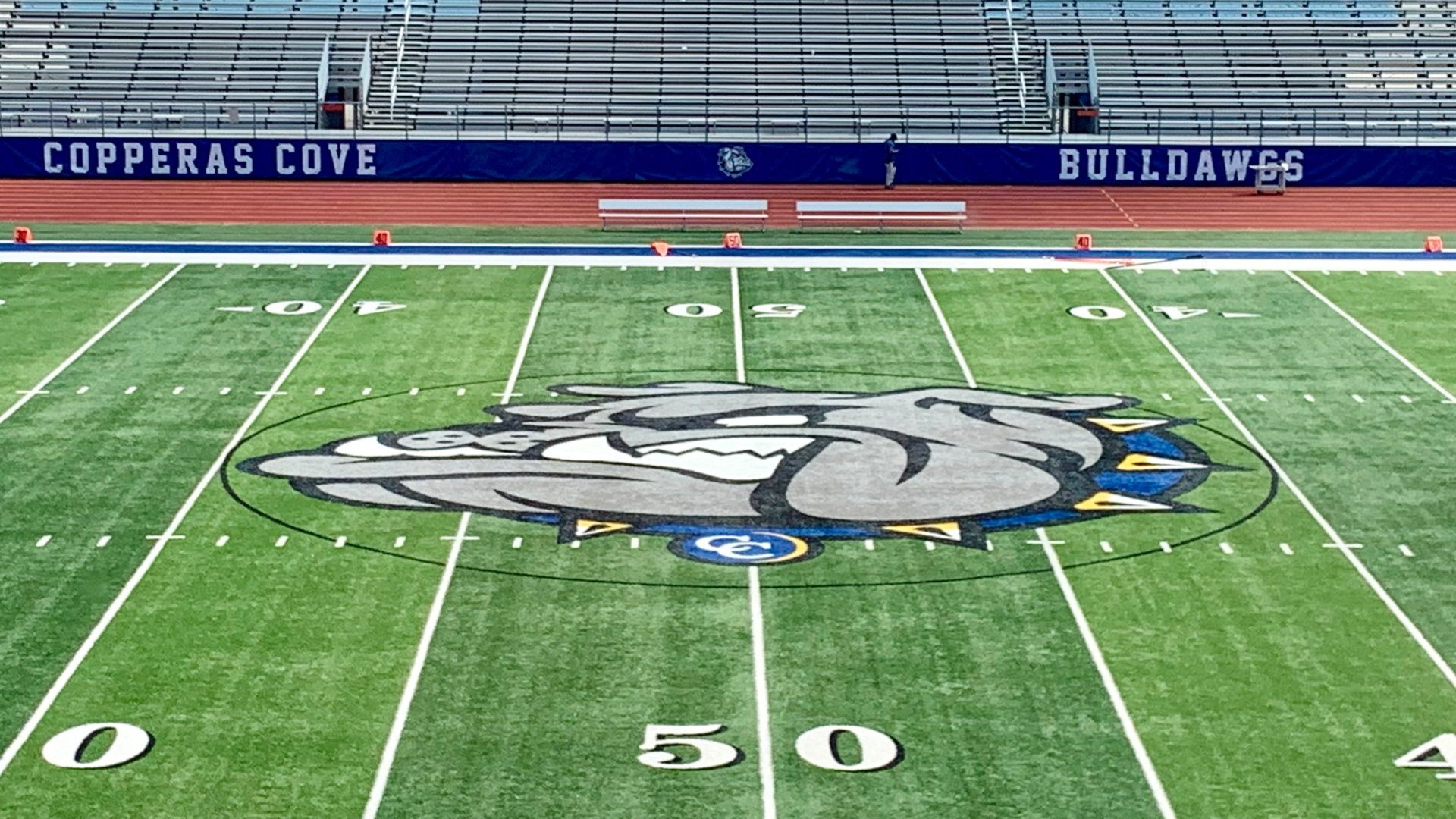 A football field showcasing a bulldog logo at the center and seating in the background.