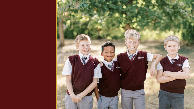 Four smiling students in maroon uniforms stand together outside