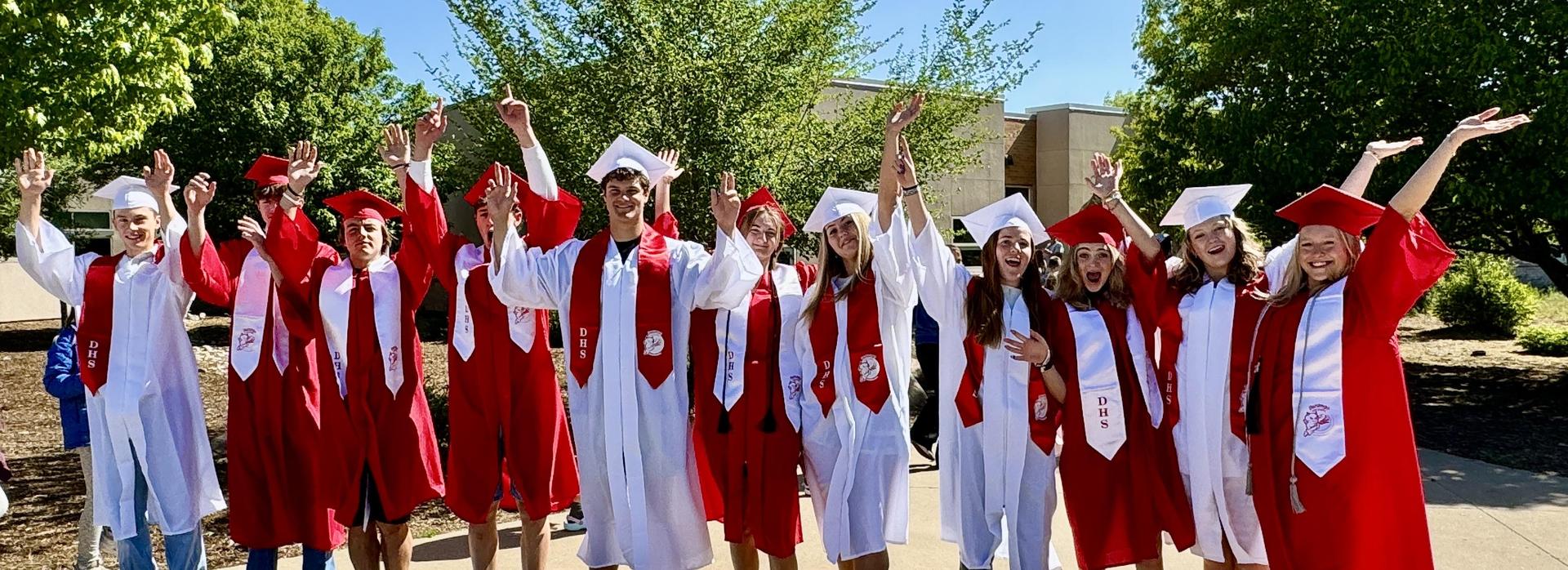 Graduates in white and red robes cheer