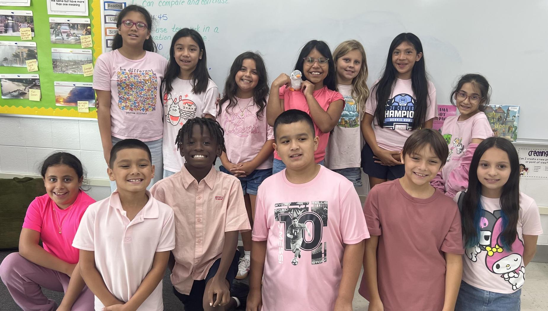 A group of students in pink clothing standing together in a classroom.