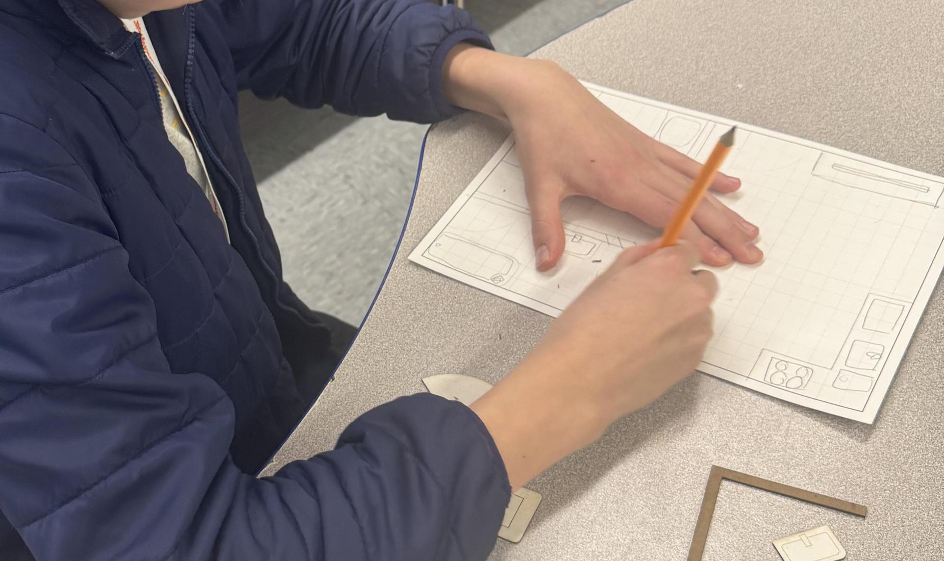 Boy creating a floor plan for an apartment.  Pieces are on table scaled to fit rooms.