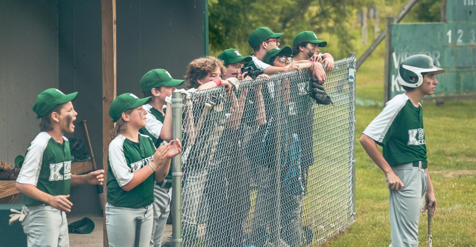 Baseball team cheering from the dugout behind a chain-link fence.