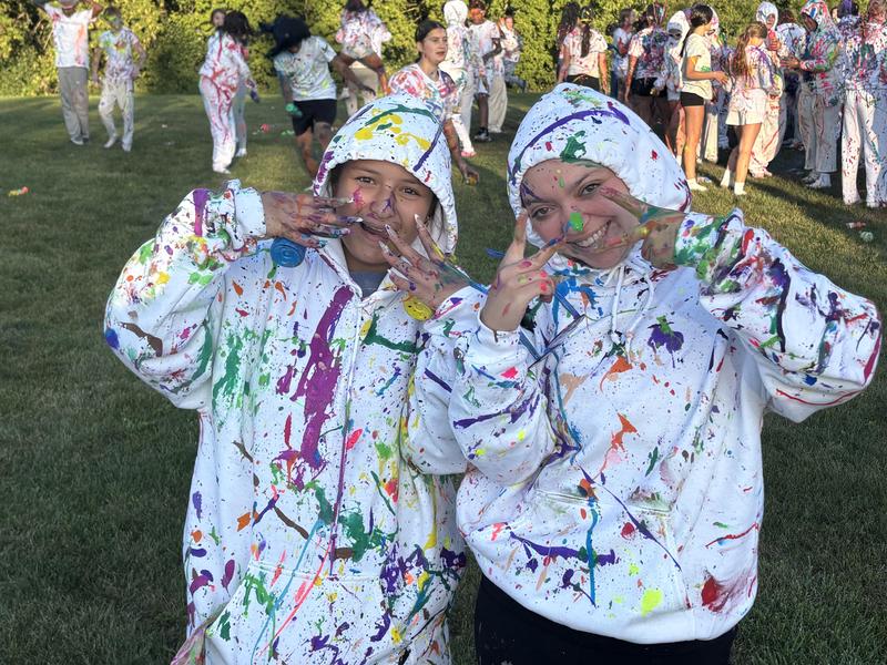 Two girls smiling and posing with colorful painted hands outdoors.