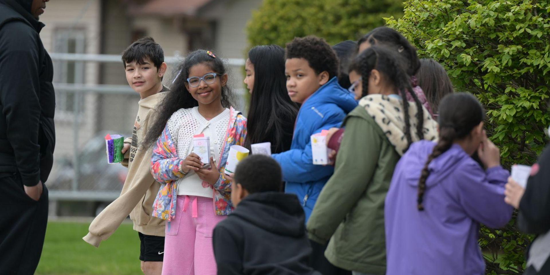 Group of children in line outside, holding juice boxes and smiling.