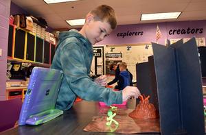 A boy positions items around a volcano model while working on a creative project.