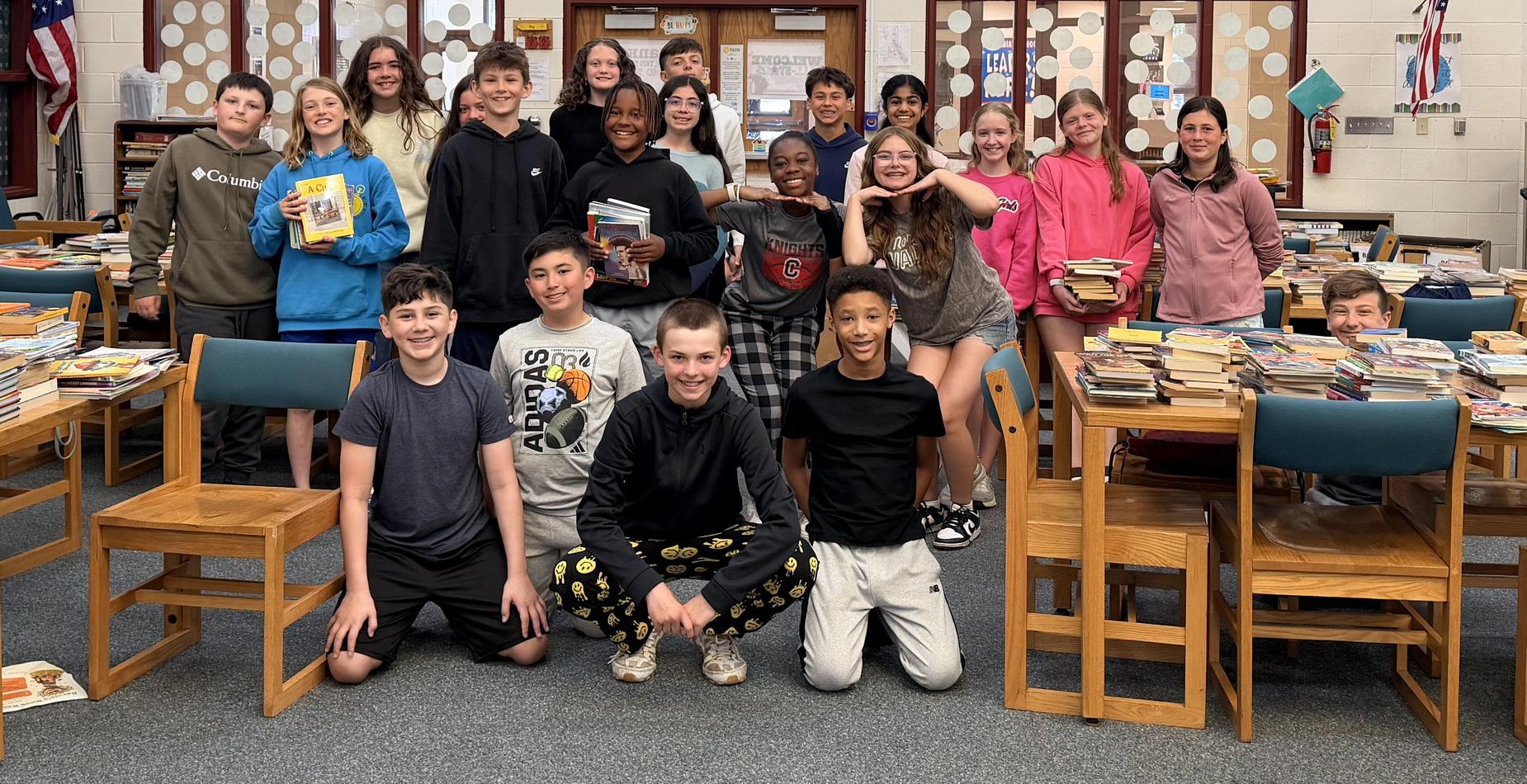 Group photo of the Hilda Walker students who sorted and boxed books that were donated in a book drive for Bernie&rsquo;s Book Bank in May. The photo is taken in the school's library and the tables around the students are filled with stacks of donated books.