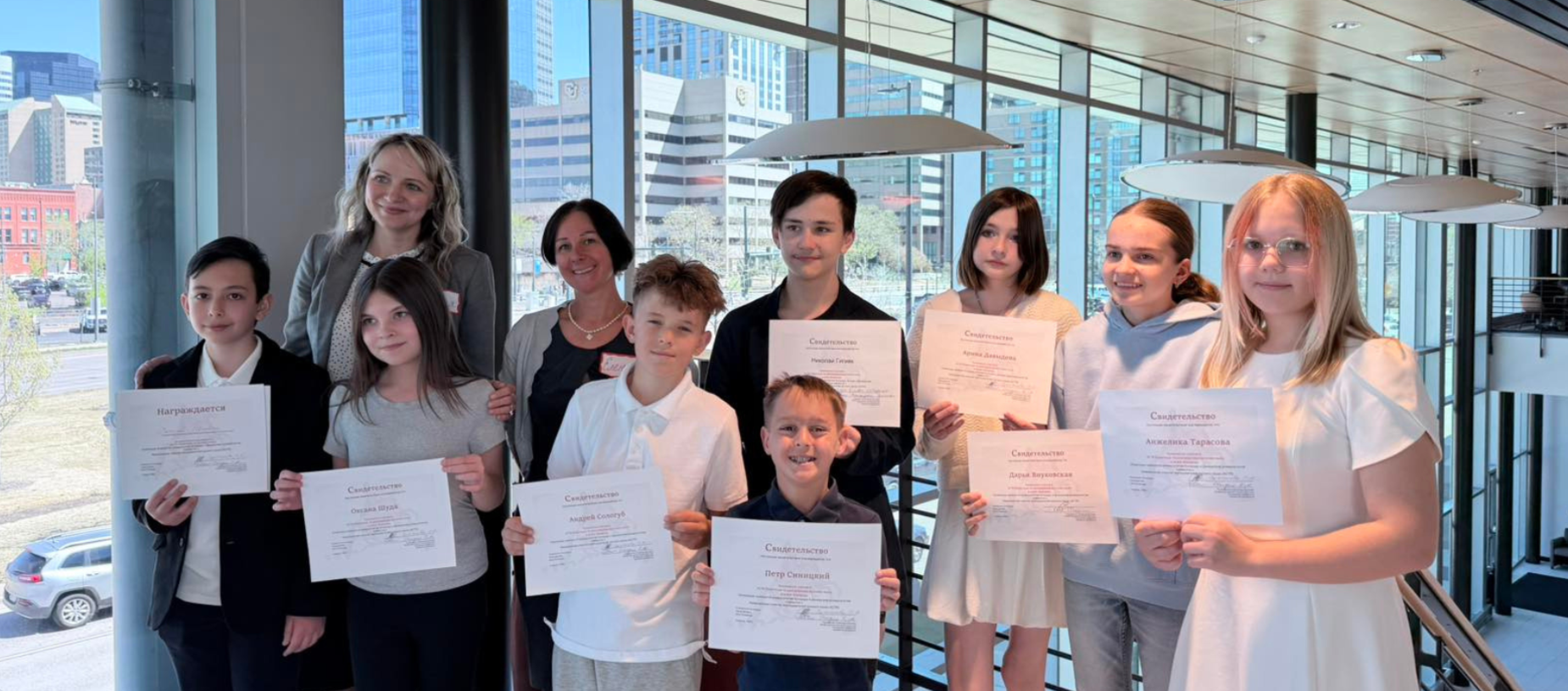 Group of children and adults holding certificates in a modern indoor setting.