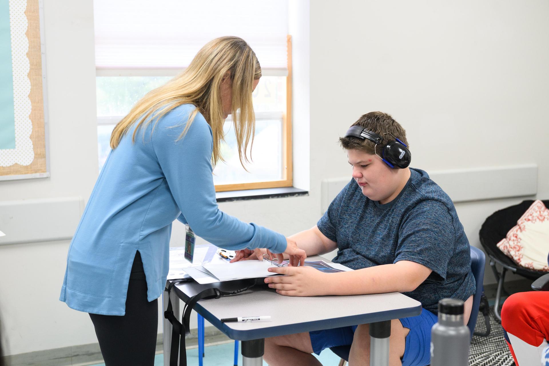 Teacher standing at student desk helping student with classwork.