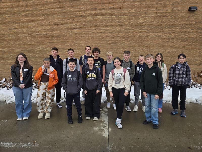 group of students standing on sidewalk in front of school